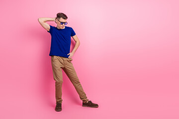 Young man wearing casual clothes stands against a pink background with a confident stance and thoughtful expression