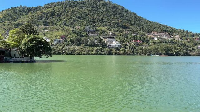 lake with islet and boat surrounded by a pathway, colorful town, forested mountains and blue sky