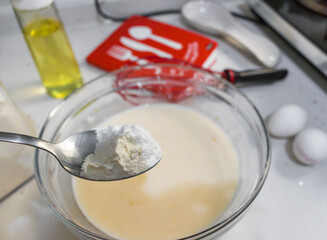 Flour is added to the pancake dough with a tablespoon.A series of home photos of the process of cooking pancakes in the kitchen. The pictures show different stages of the culinary process: kneading