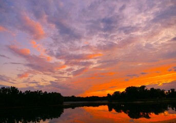 Colorful sunset on the peaceful lake with clouds and trees silhouettes