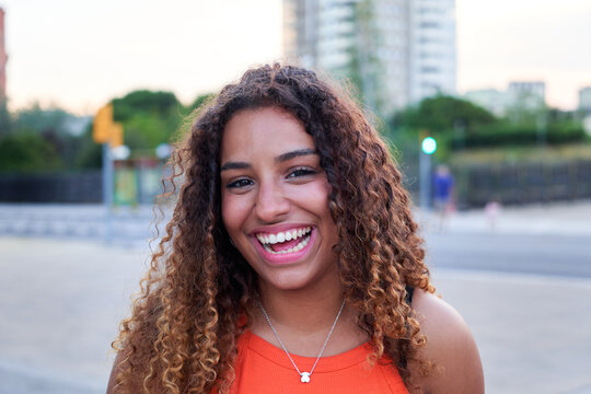 Portrait of a cheerful young African American woman looking at camera with big smile, standing outdoors in a city environment.