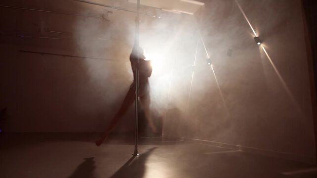 Static view of a young woman pole dancing in a smoky stage