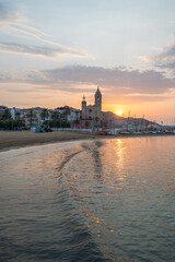 Sunrise illuminating Sitges beach and Sant Bartomeu church