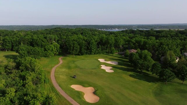 Aerial dolly of golf course showing sand bunkers and striped green mowing lines as golf cart drives onto path
