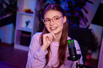 Young female content creator with microphone working in cozy home studio during evening with warm...