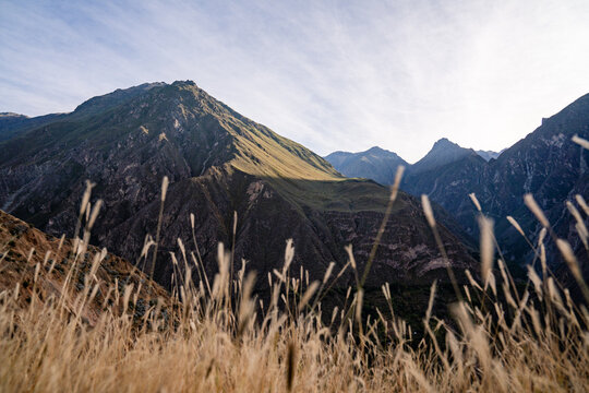Weitläufige Berglandschaft am Colca Canyon in Peru mit Gräsern im Vordergrund und Sonne - Powered by Adobe