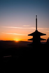 Silhouette of a Japanese pagoda at sunset over a landscape.