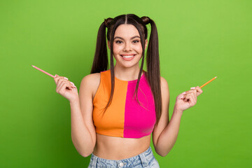 Cheerful young woman in colorful casual fashion holding pencils against a vibrant green background