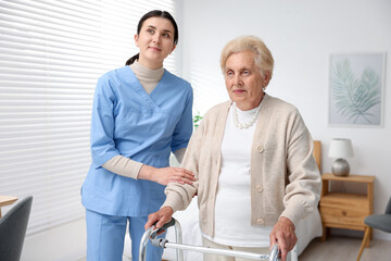 Obraz premium Nurse assisting senior woman with walking frame indoors. Home health care service