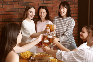 Group of happy friends clinking glasses of beer at table indoors