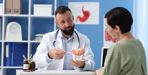 Gastroenterologist with model of stomach consulting woman in clinic