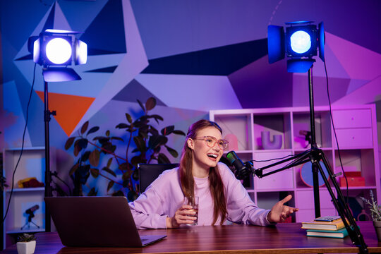 Popular Young female vlogger hosting a live podcast in vibrant neon studio