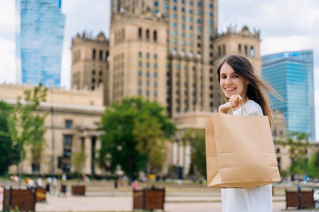 Fototapeta premium Smiling young woman with eco-friendly paper shopping bag in the city