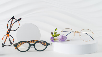 Three pairs of plastic eyeglass frames on white background with flowers. Eyewear fashion collection...