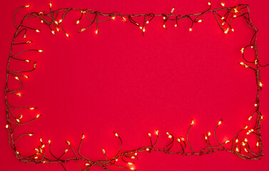 Christmas string lights glowing on red background, festive holiday garland decoration, top view...