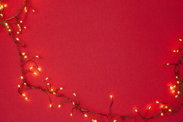 Christmas string lights glowing on red background, festive holiday garland decoration, top view...