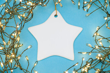 Star ceramic ornament framed by glowing Christmas string lights, flat lay festive holiday decor on...