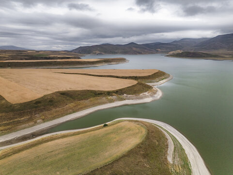 Aerial view of the Spandarian Reservoir's waters meeting the arid land, creating a striking contrast under a cloudy sky, Spandarian Reservoir, Syunik, Armenia.