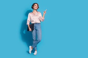 Charming young woman in a satin pink blouse pointing and smiling against a vibrant blue background