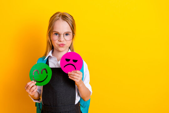 Young schoolgirl in uniform holding emoji mood signs on yellow background representing education and emotions
