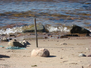 Rusty metal rod on sandy beach with stones and waves
