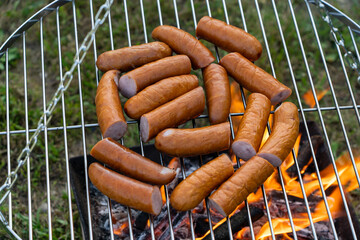 A close-up of a fresh, uncooked sausage smoking directly over the fire. Perfect for barbecue lovers...