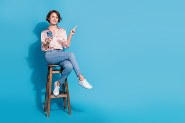 Charming young businesswoman in pink satin blouse pointing with confidence against vibrant blue...
