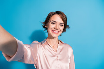 Young woman in pink satin blouse enjoying joyful moments with charming smile against blue background
