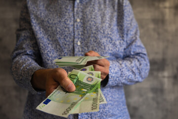 A young man in a blue shirt holds 100 euro banknotes in his hands, the man spends money