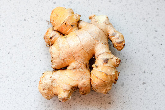 A piece of fresh ginger root with a knobby, tan surface is placed on a gray speckled countertop. The