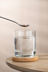 A spoon of Himalayan salt is being added to a glass of drinking water.