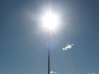 Bright sun flare above tall spire in blue sky

