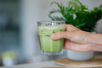 hand of woman holding a glass of iced matcha latte on table at cafe.
