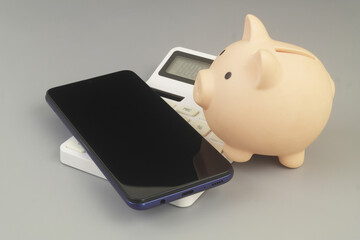 Piggy bank and smartphone on calculator on grey background.