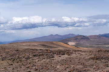 Weite, karge Landschaft der peruanischen Anden mit einem kleinen Steinhaufen unter einem dramatischen Himmel