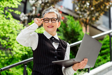 Professional woman wearing stylish formalwear working outdoors with laptop during a sunny day in an...