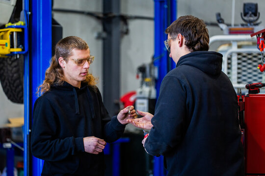 Young male mechanic handing over a tool part to his workmate