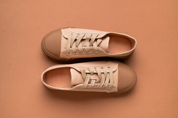 Stylish fashionable fabric beige sneakers on brown background flat lay top view. Trendy women's or men's sports casual shoes, minimalist background with sneakers with space for text