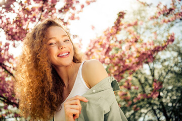 Lovely female enjoying a sunny spring day outdoors among flowering trees in nature, showcasing...