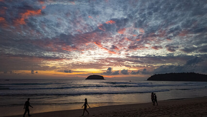 Golden Embrace above Kata beach.
The setting sun paints the horizon with golden light, reflecting across gentle waves as silhouettes of beachgoers stroll peacefully along the shoreline.