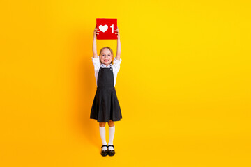 Happy schoolgirl in uniform holding a placard with love icon on yellow background, smiling and...