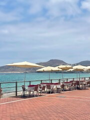 Seaside café tables with umbrellas along a sunny promenade — perfect spot for a summer getaway.