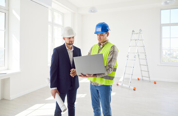Construction engineer and architect colleagues looking at project online on laptop, blueprints,...