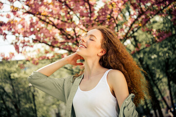 Young woman with curly red hair enjoying a springtime walk under blossoming trees