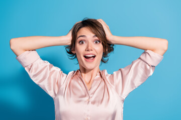 Surprised young woman in stylish pink blouse against blue background, expressing joy with hands on...