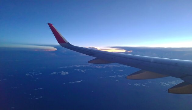 Fototapeta Airplane wing seen from above, with a view of clouds and the earth below.
