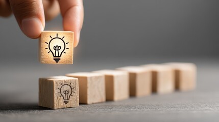 Hand placing illuminated lightbulb cube onto row of wooden blocks symbolizing idea generation and innovation solutions