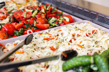 A close-up of fresh salads on a buffet counter, including a pickled cabbage slaw and a tomato salad