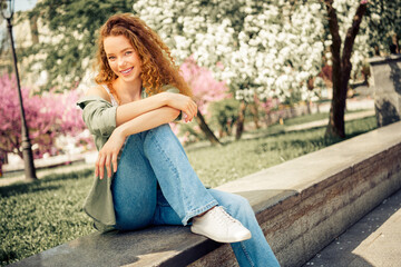 Young woman enjoying a sunny day in a blooming park, surrounded by beautiful flowers and greenery,...