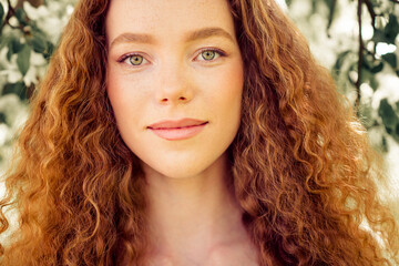 Charming young woman with curly red hair enjoying a peaceful sunny day outdoors